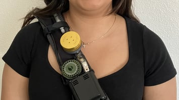 A photograph of a person wearing a UPAS v2.1 PLUS on a cross-body backpack strap.