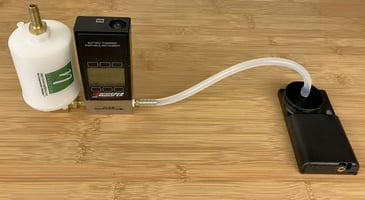 A photograph of a UPAS v2.0 with an external flow meter connected to the UPAS inlet