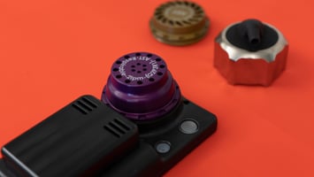 A photograph of a UPAS v2.1 PLUS with a respirable PM inlet installed. A PM10 inlet and a flow check adapter are also sitting nearby in the image.