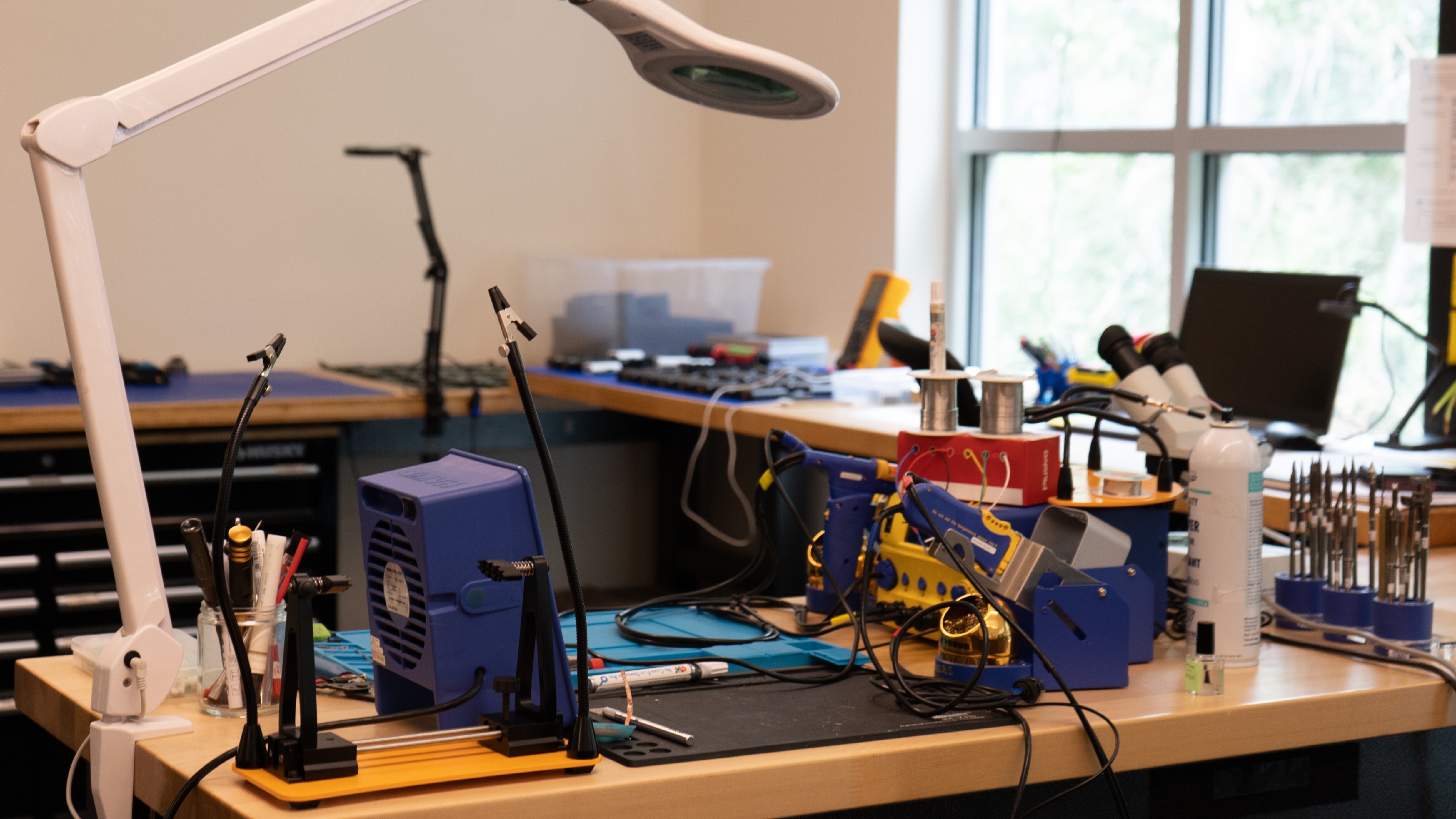 A photograph of a workstation with a multimeter, computer, and soldering iron.